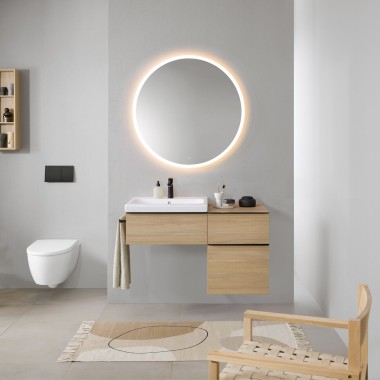 Kopalnica s sivimi stenami, lesenim pohištvom za kopalnico Geberit in okroglim ogledalom z osvetlitvijo Geberit Option